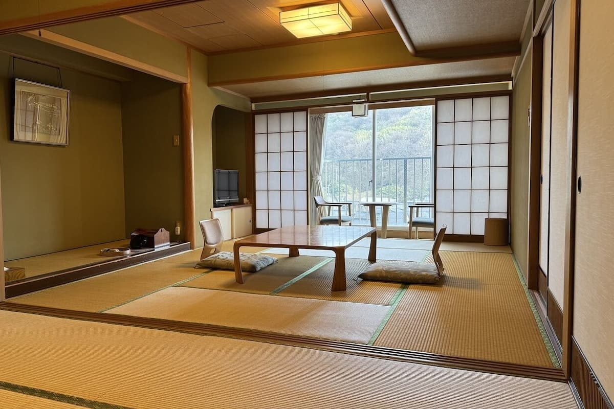 Una habitación japonesa tradicional con suelo de tatami, puertas correderas y vistas a un bosque.