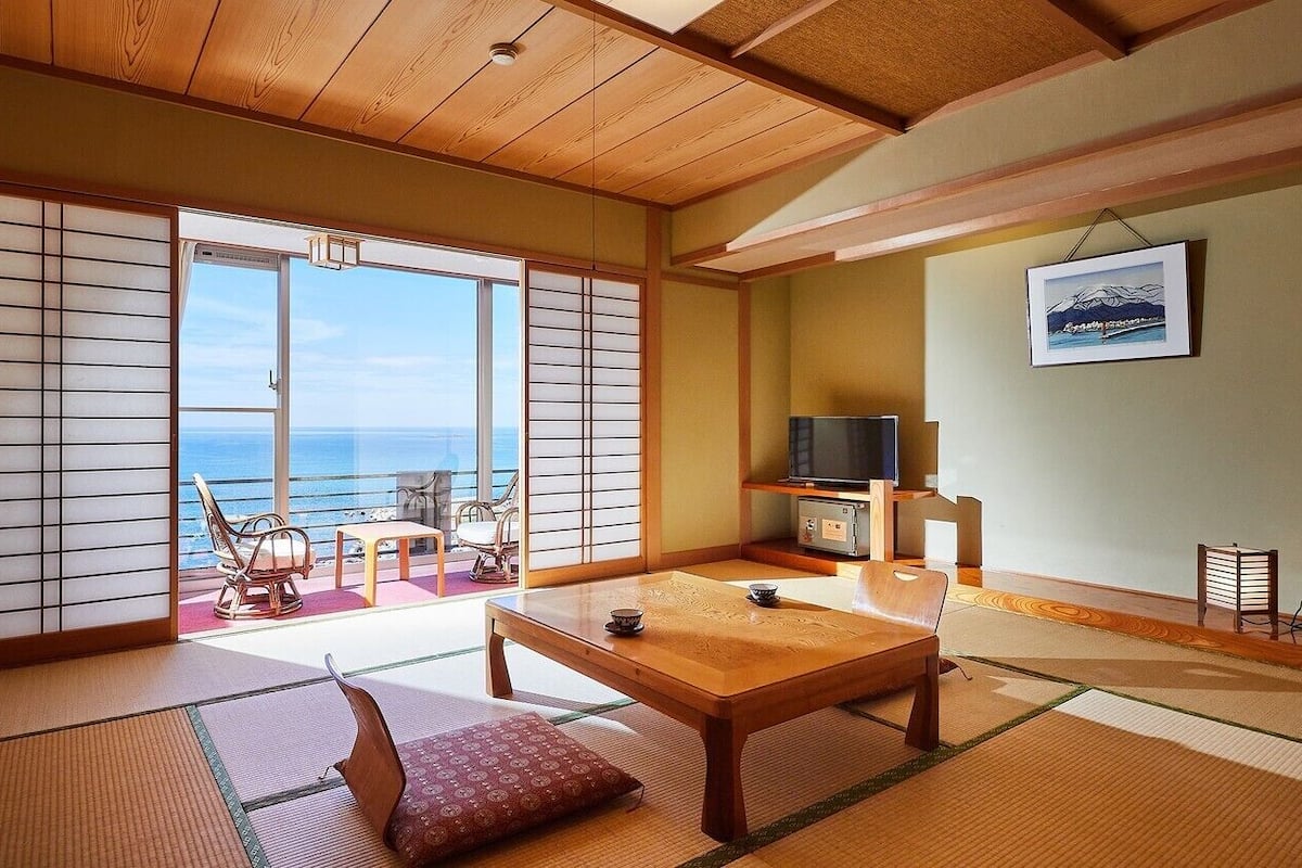 Una habitación japonesa tradicional con suelo de tatami, un shoji corredizo, una mesa de madera, un televisor y vistas al mar.