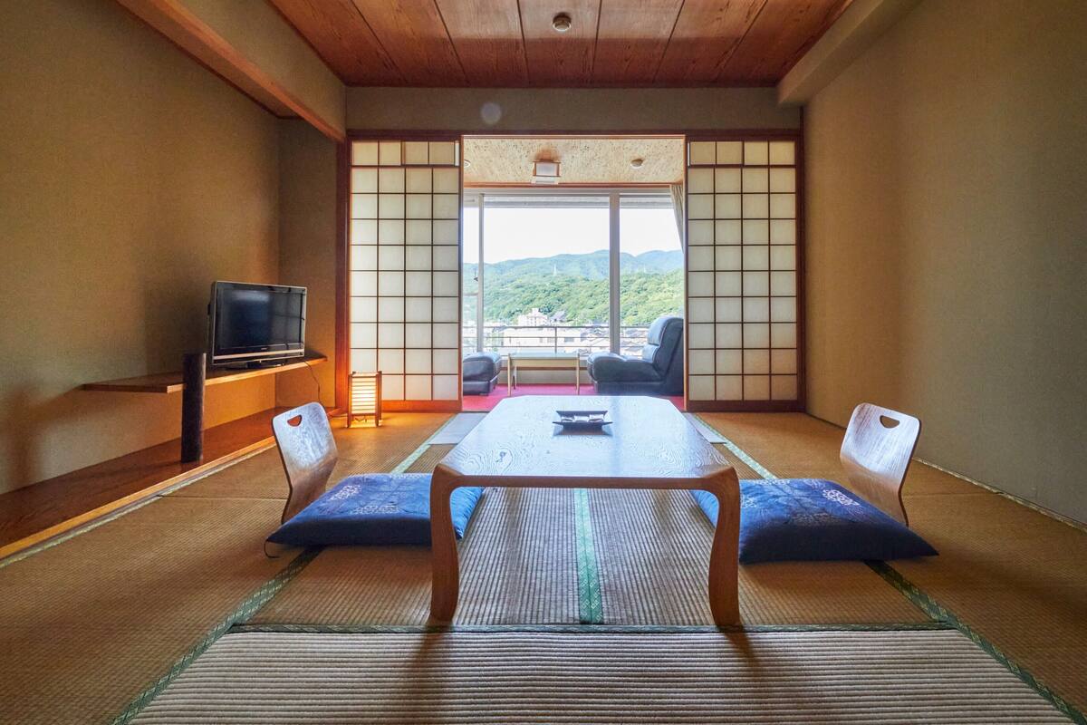 Una habitación japonesa tradicional con suelo de tatami, una mesa baja y un televisor en un estante.