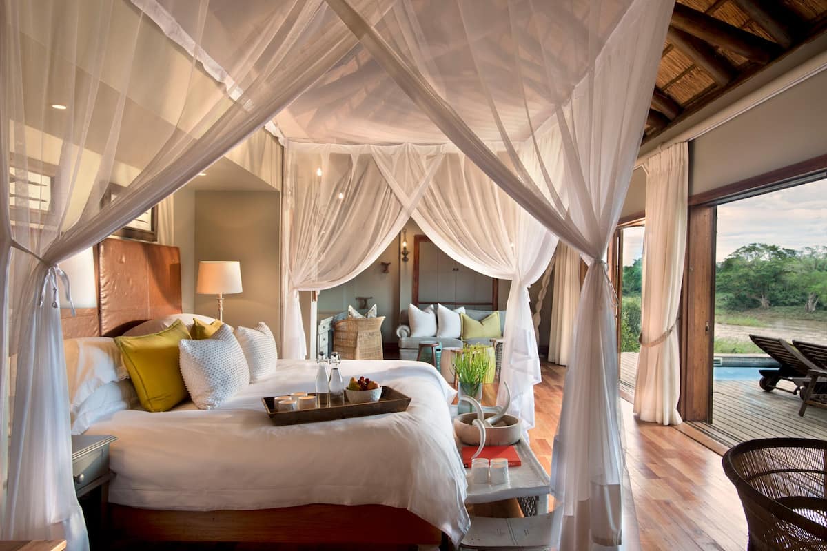 A bedroom with a canopy bed, bedside table with a tray, and a view of the outdoors.