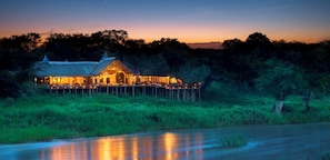 A lodge with a thatched roof, a deck, and a view of the surrounding forest. - Lion Sands Narina Lodge (Mpumalanga-SKUKUZA)