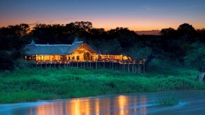 A lodge with a thatched roof, a deck, and a view of the surrounding forest.