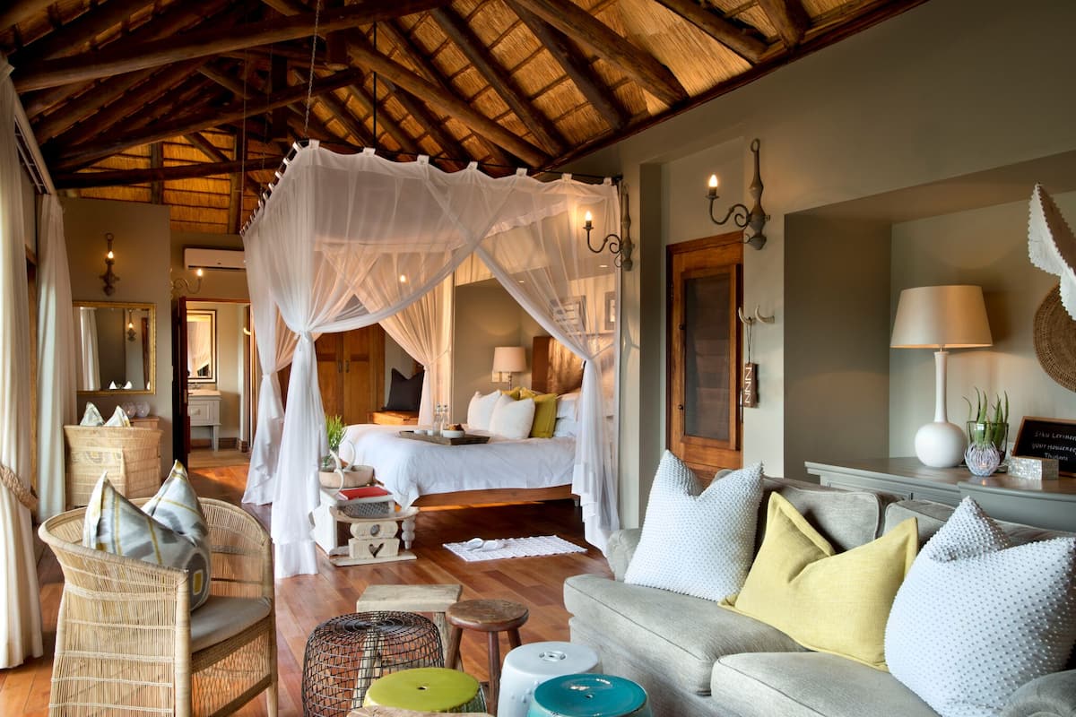 A bedroom with a canopy bed, a sitting area with a sofa and chairs, and a dining area with a table and chairs.
