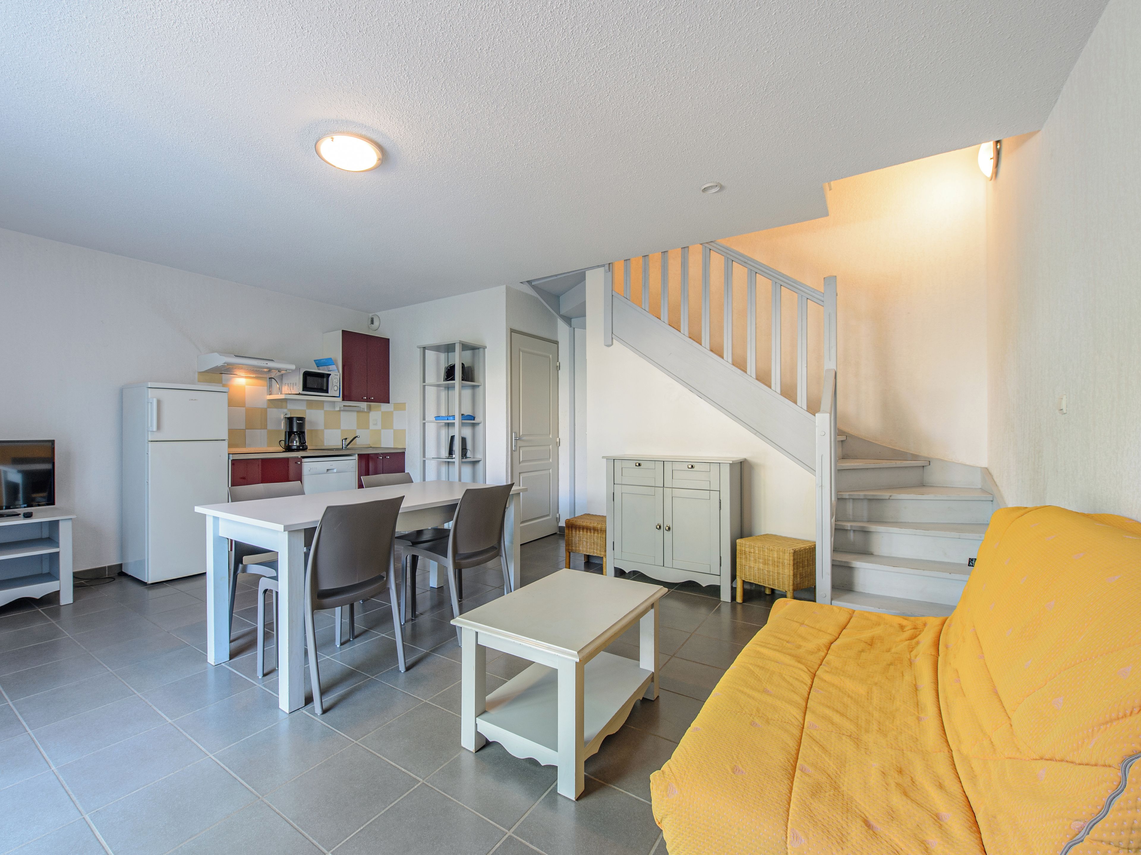 A compact living space with a dining area, kitchenette, and a staircase leading to an upper level.