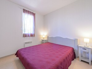 A single-bed room with a red bedspread, two bedside tables with lamps, a window with curtains, and a radiator. - Les Demeures du Ventoux - Vacanceole (Aubignan)