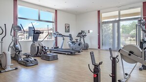 A spacious gym with various cardio and strength training equipment, large windows, and a wooden floor. - Les Demeures du Ventoux - Vacanceole (Aubignan)