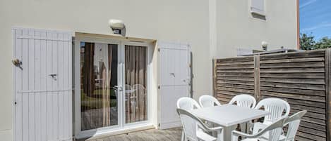 A patio with a white table and chairs, a sliding glass door, and a wooden deck.