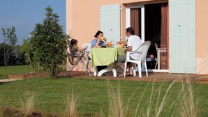 A dining area with a table set for four, outdoor seating, and a building with a door and window.