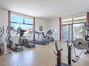 Un gimnasio con diferentes máquinas de ejercicio, amplias ventanas y vistas al exterior.