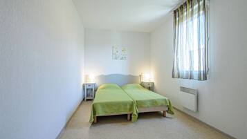 A bedroom with two beds, bedside lamps, a radiator, and a window with curtains.