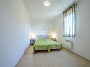 Un dormitorio con dos camas, lámparas de noche, un radiador y una ventana con cortinas.