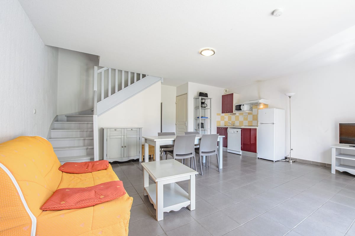 Un apartament modern amb saló, menjador, cuina i una escala.
