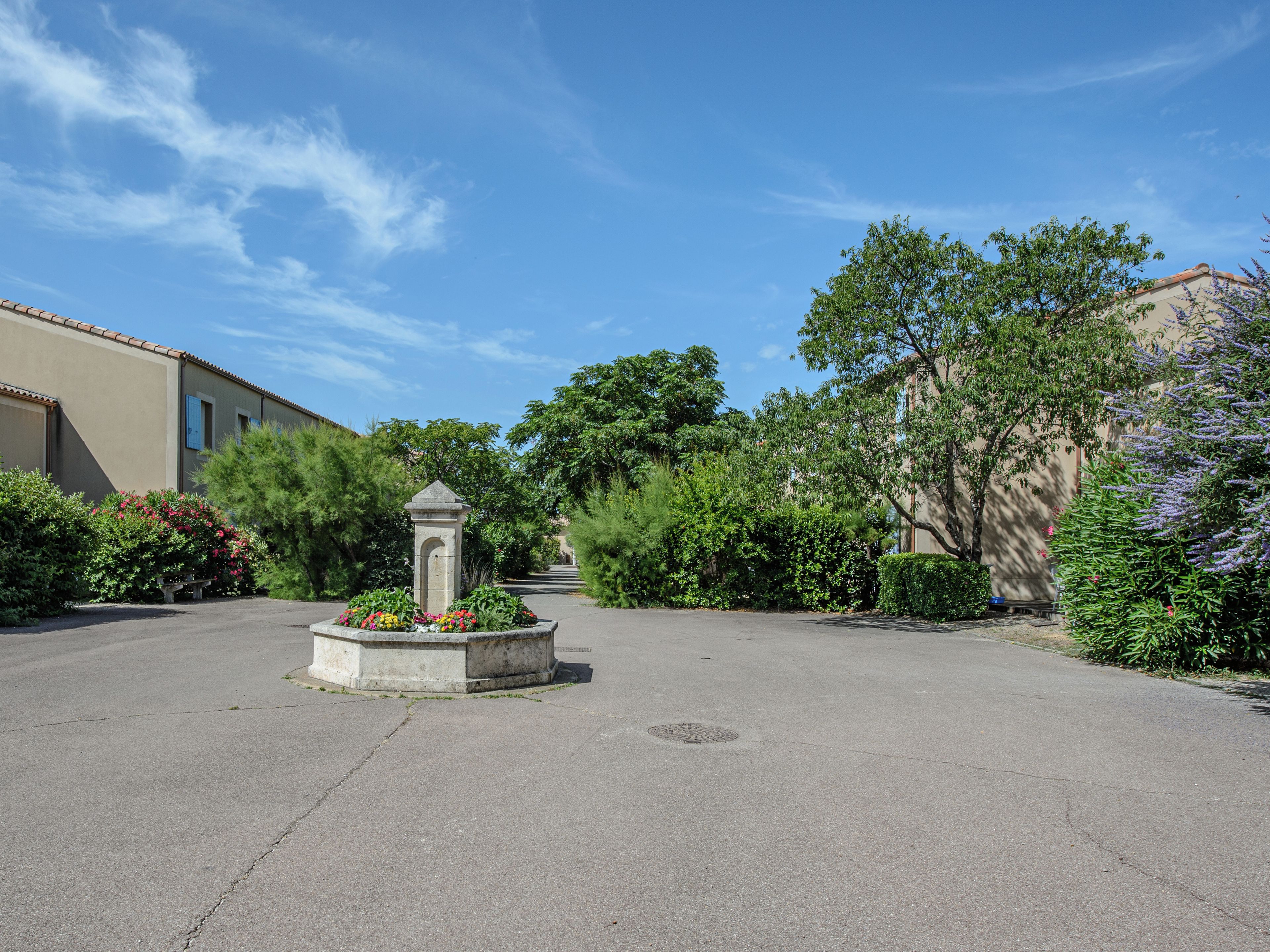 A courtyard with a central fountain, surrounded by lush greenery and a building with a tiled roof.