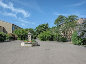 A courtyard with a central fountain, surrounded by lush greenery and a building with a tiled roof. - Les Demeures du Ventoux - Vacanceole (Aubignan)