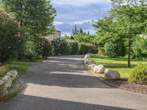 A gravel pathway flanked by lush greenery and large rocks, leading to a building with a light-colored facade. - Les Demeures du Ventoux - Vacanceole (Aubignan)