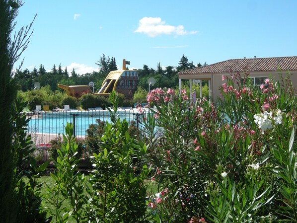 A pool area with a slide, surrounded by greenery and a building with a tiled roof. - Les Demeures du Ventoux - Vacanceole (Aubignan)