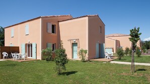 A two-story building with a flat roof, a covered patio with a table and chairs, and a small garden area with a tree and shrubs. - Les Demeures du Ventoux - Vacanceole (Aubignan)