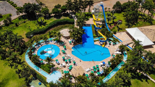 An aerial view of a water park with multiple pools, slides, and a large central pool surrounded by lounge areas and palm trees.