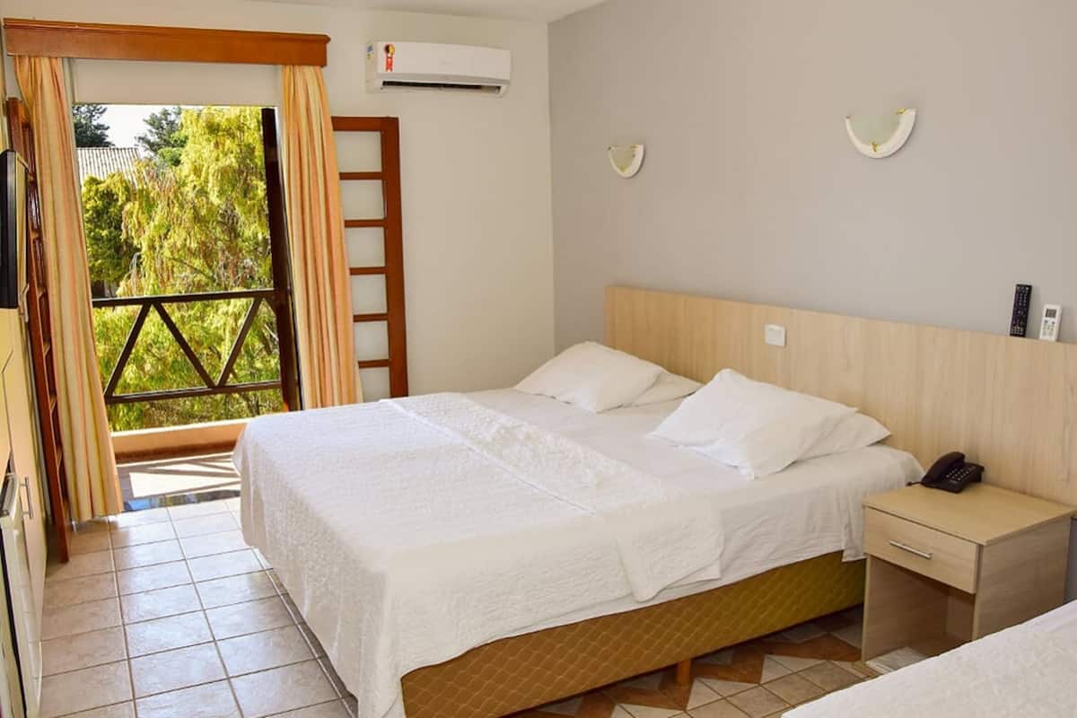 Une chambre d’hôtel avec un lit, une table de chevet avec un téléphone, une lampe fixée au mur et une vue sur la verdure à l’extérieur.