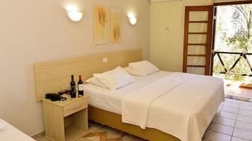 A hotel room with a wooden bed, white linens, a bedside table with wine bottles, and a view of greenery through a door.