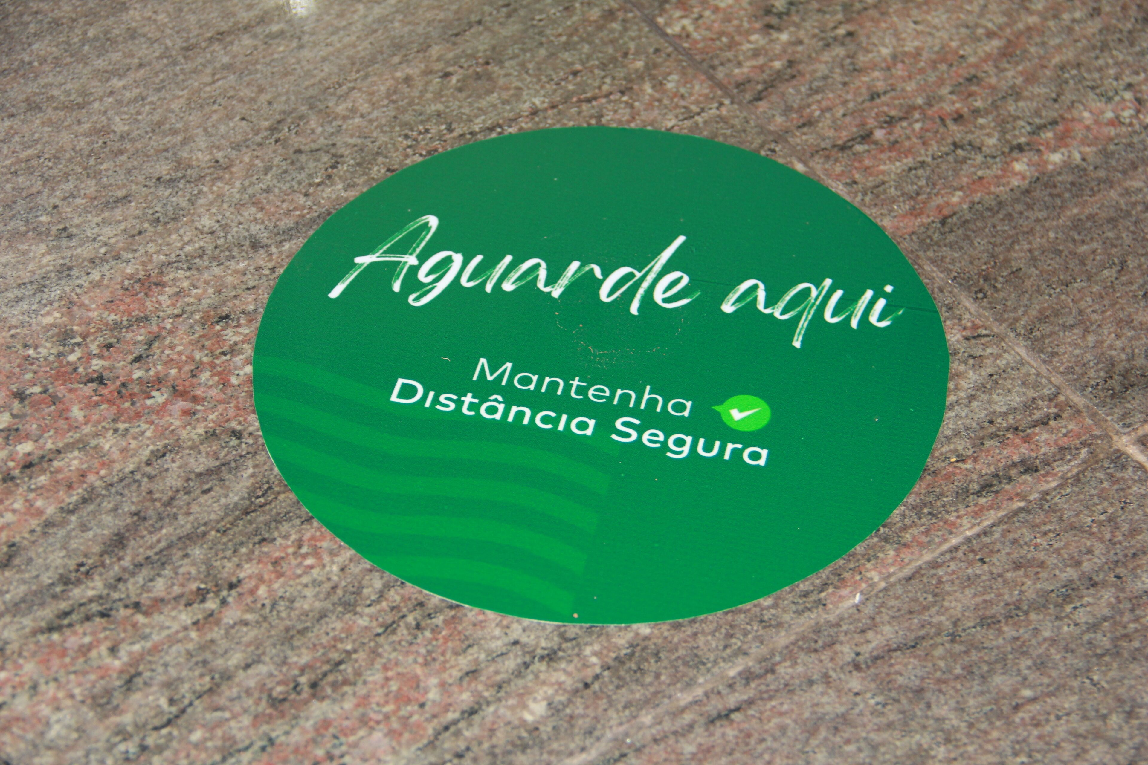 A green circular sign with text in Portuguese, placed on a stone surface.