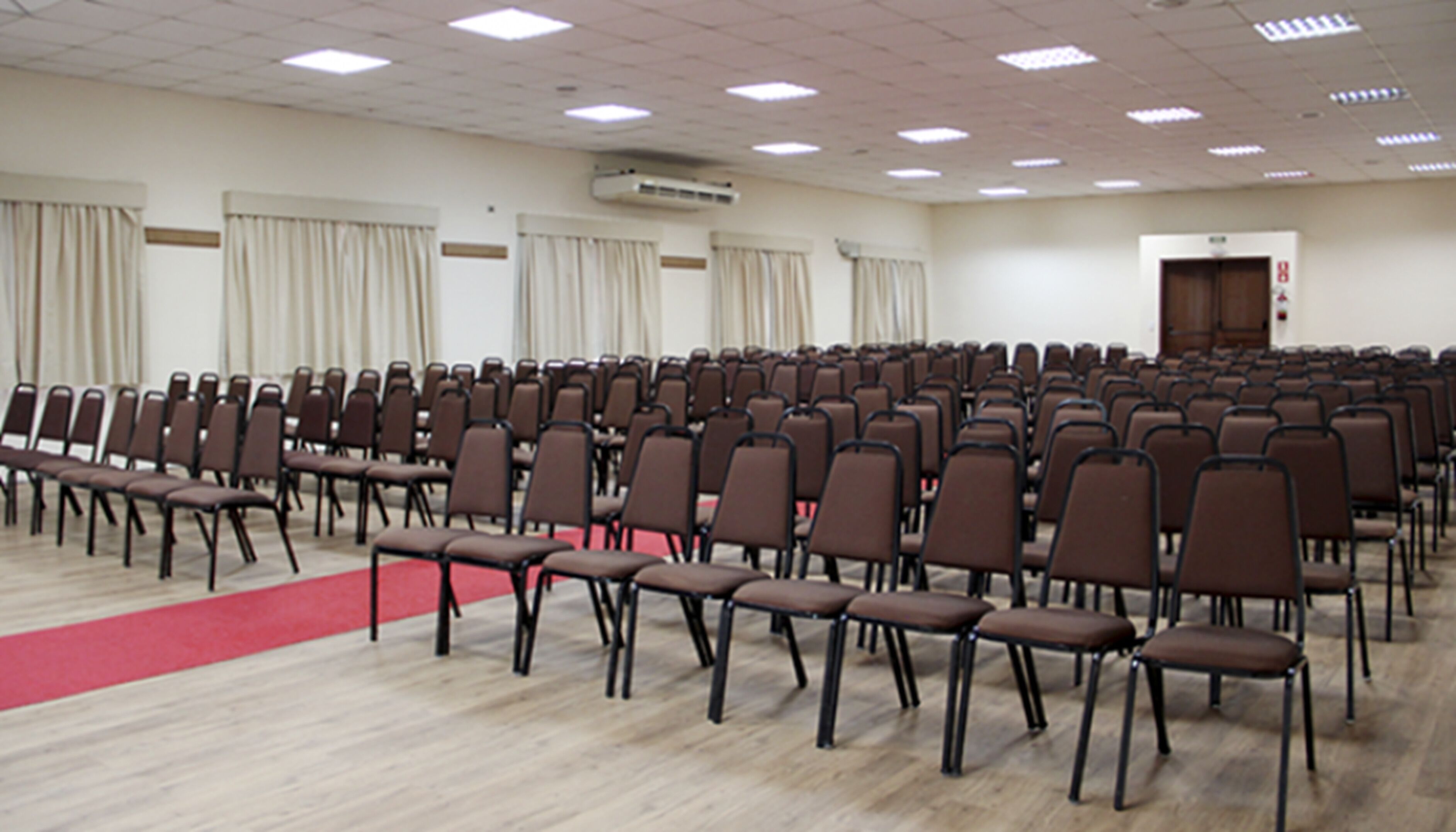 A conference room with rows of chairs, a red carpet, and an air conditioning unit on the ceiling.