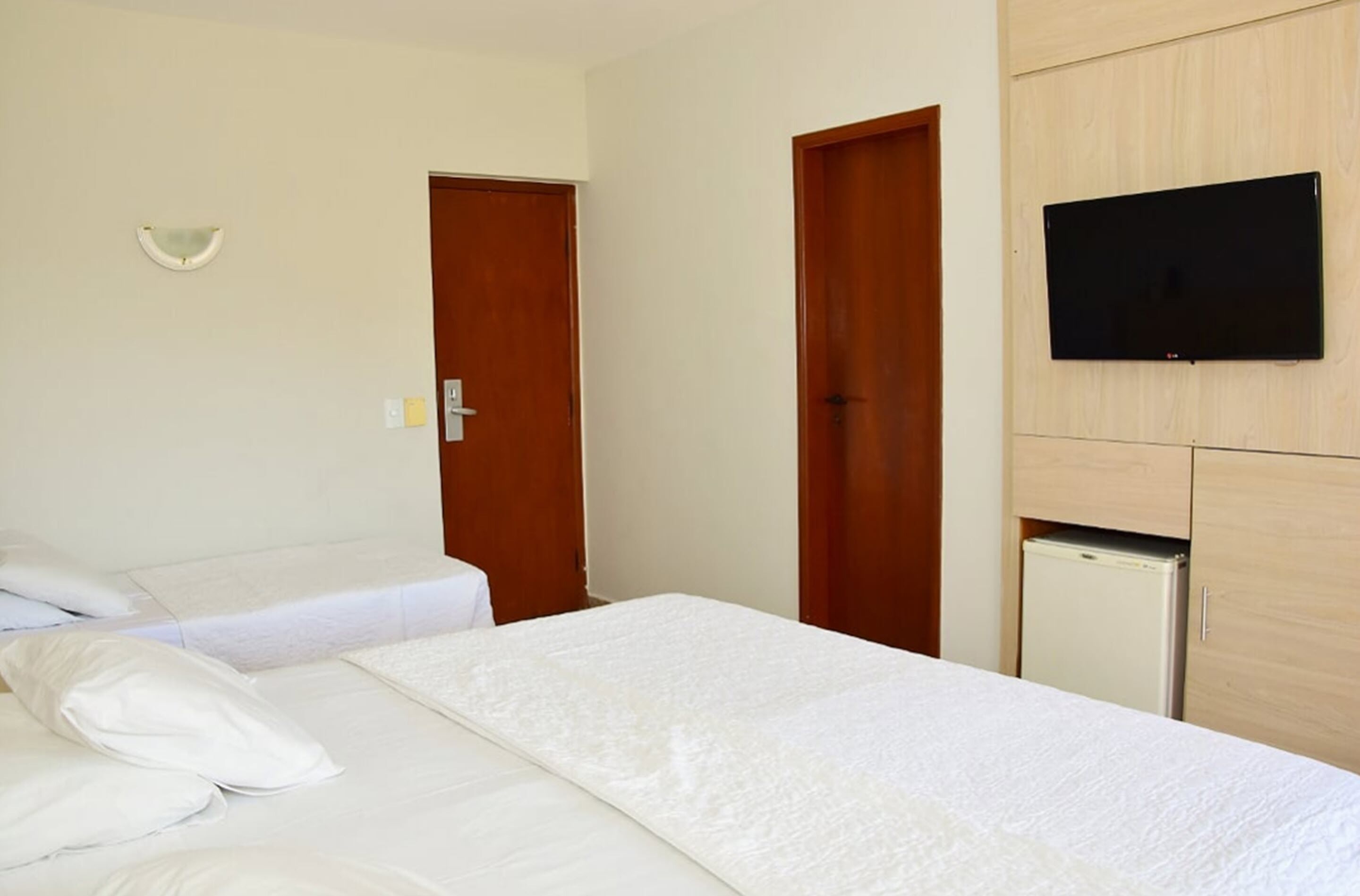 Habitació d'hotel amb llit, televisió penjada a la paret i nevera petita.