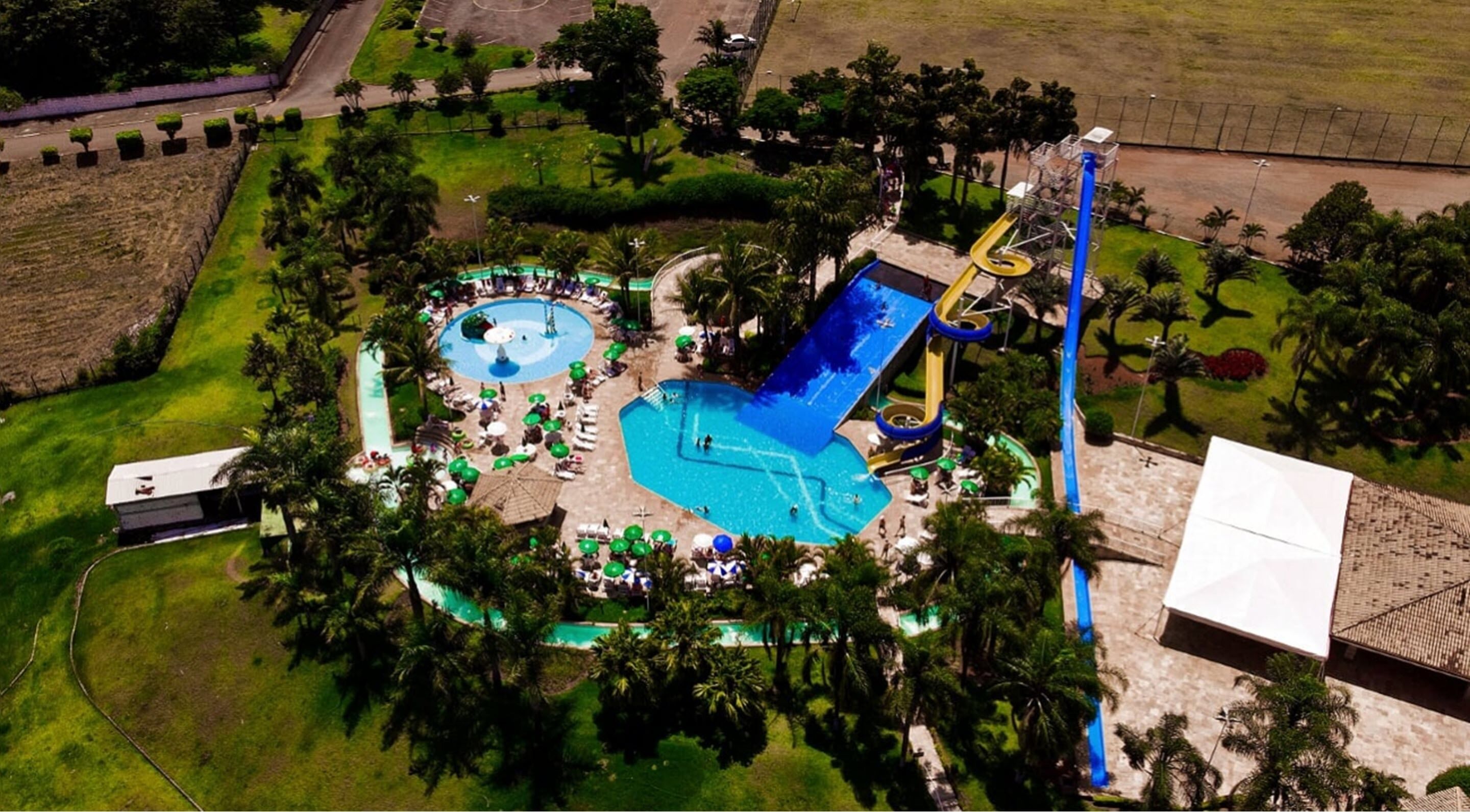 An aerial view of a resort with multiple swimming pools, a water slide, and lush greenery.