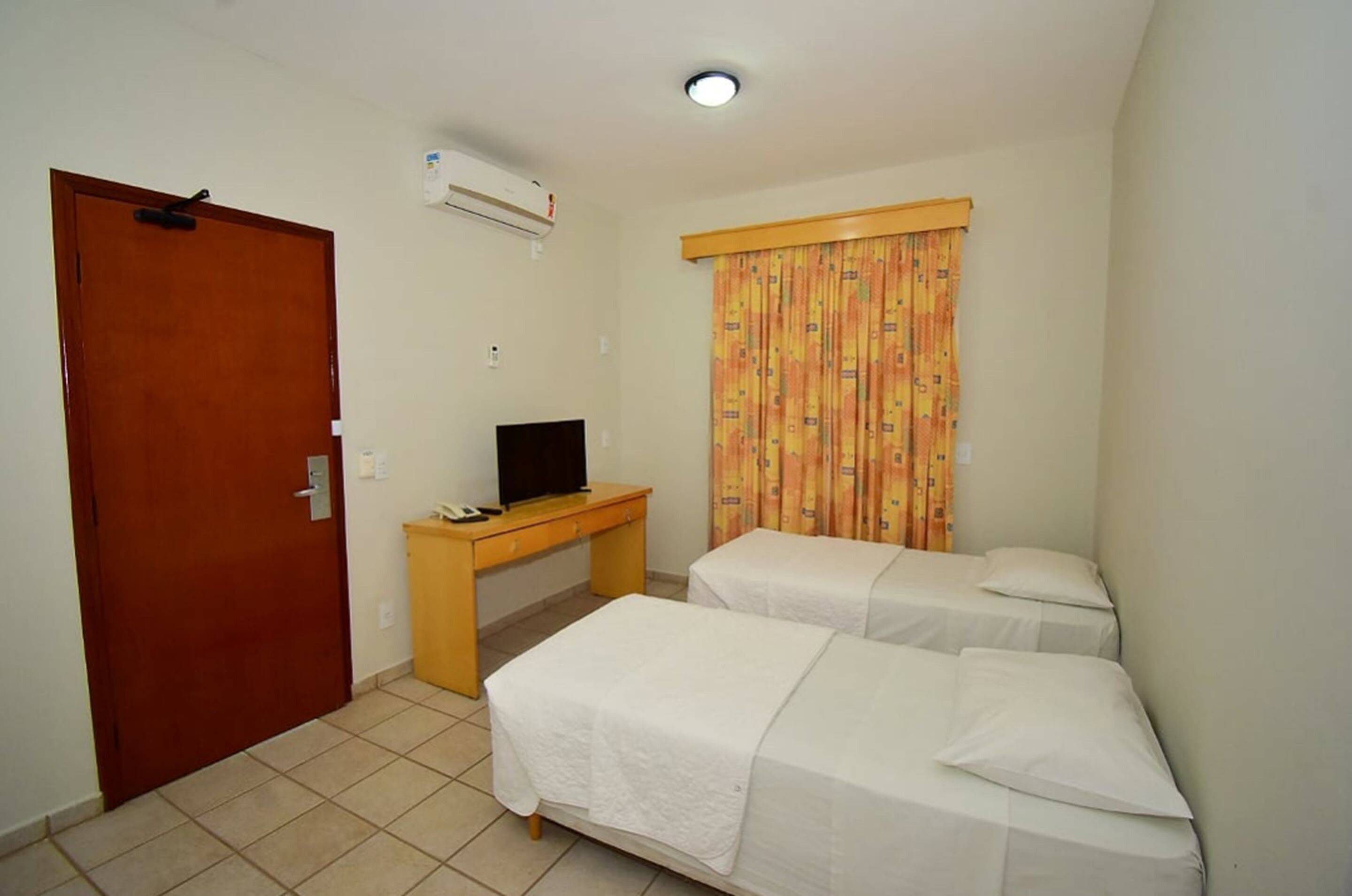 Habitación de hotel con dos camas individuales, un escritorio de madera con televisor y una puerta.