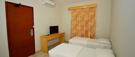 Habitación de hotel con dos camas individuales, un escritorio de madera con televisor y una puerta.