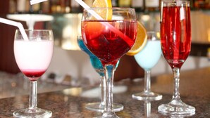 A bar with various cocktails and a background of shelves stocked with bottles.