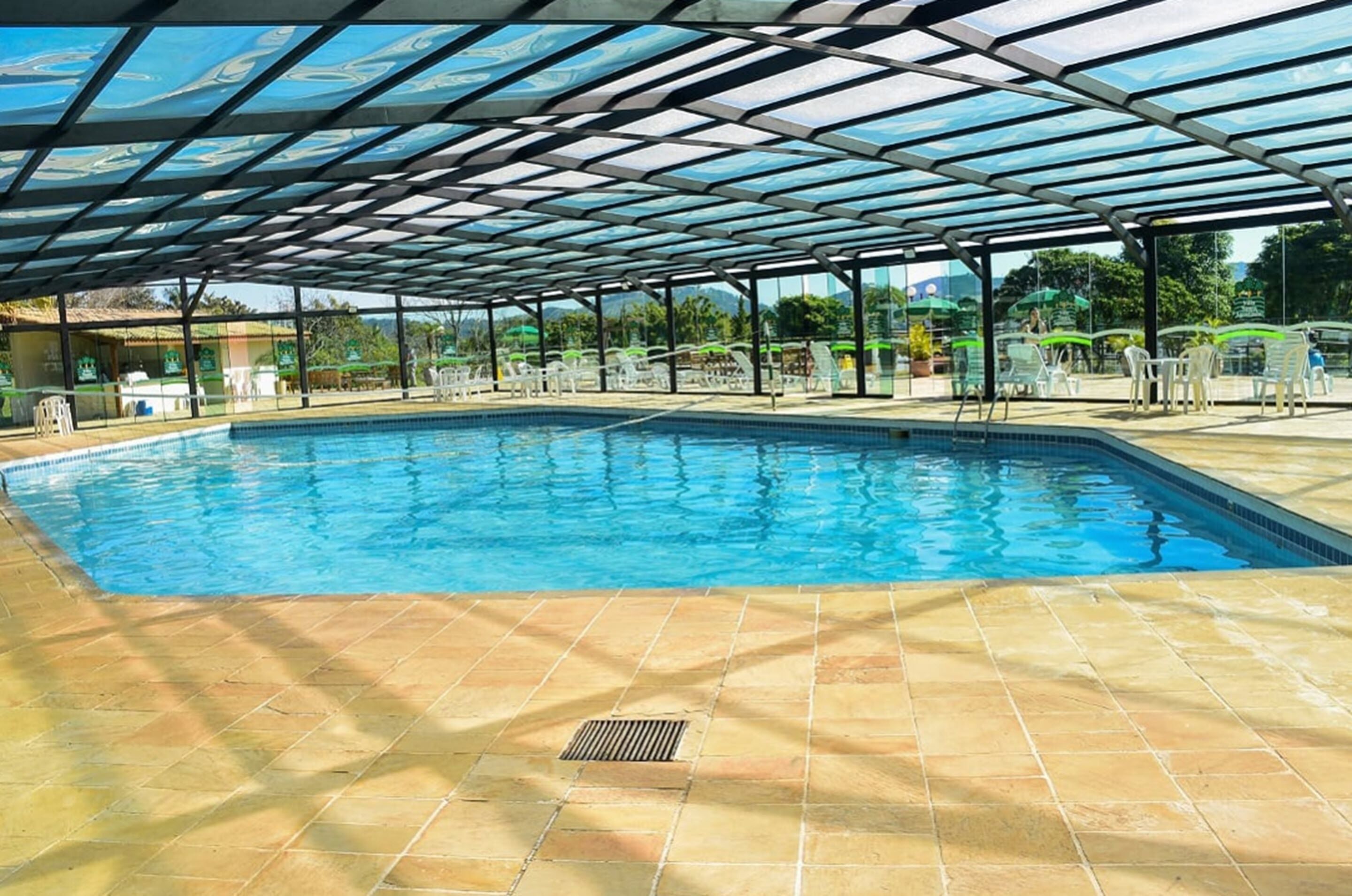 Piscina com cobertura de vidro, rodeada por espreguiçadeiras e mesas.