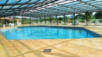Piscina com cobertura de vidro, rodeada por espreguiçadeiras e mesas.