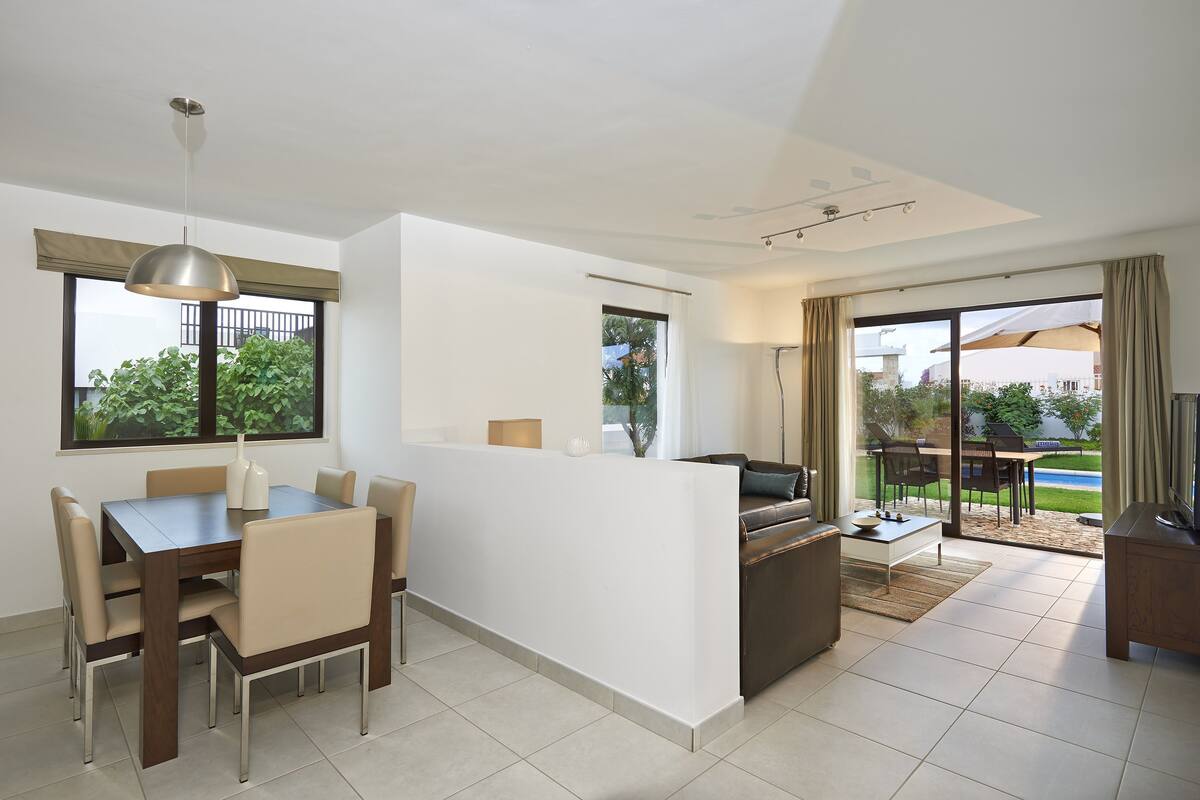 A modern living room with a dining area, a sofa, and a TV.