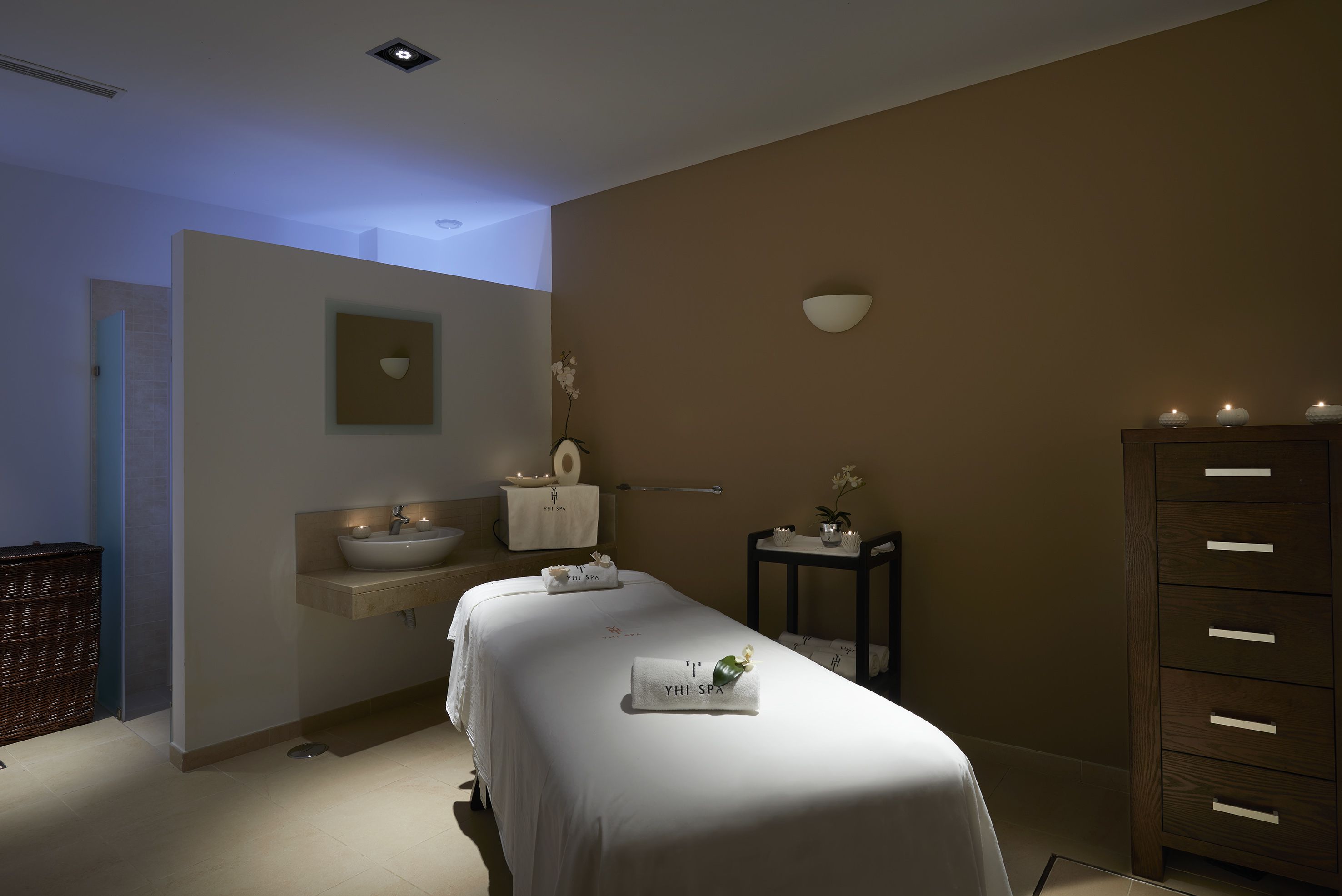 A spa room with a bed, a sink, a mirror, and a cabinet.