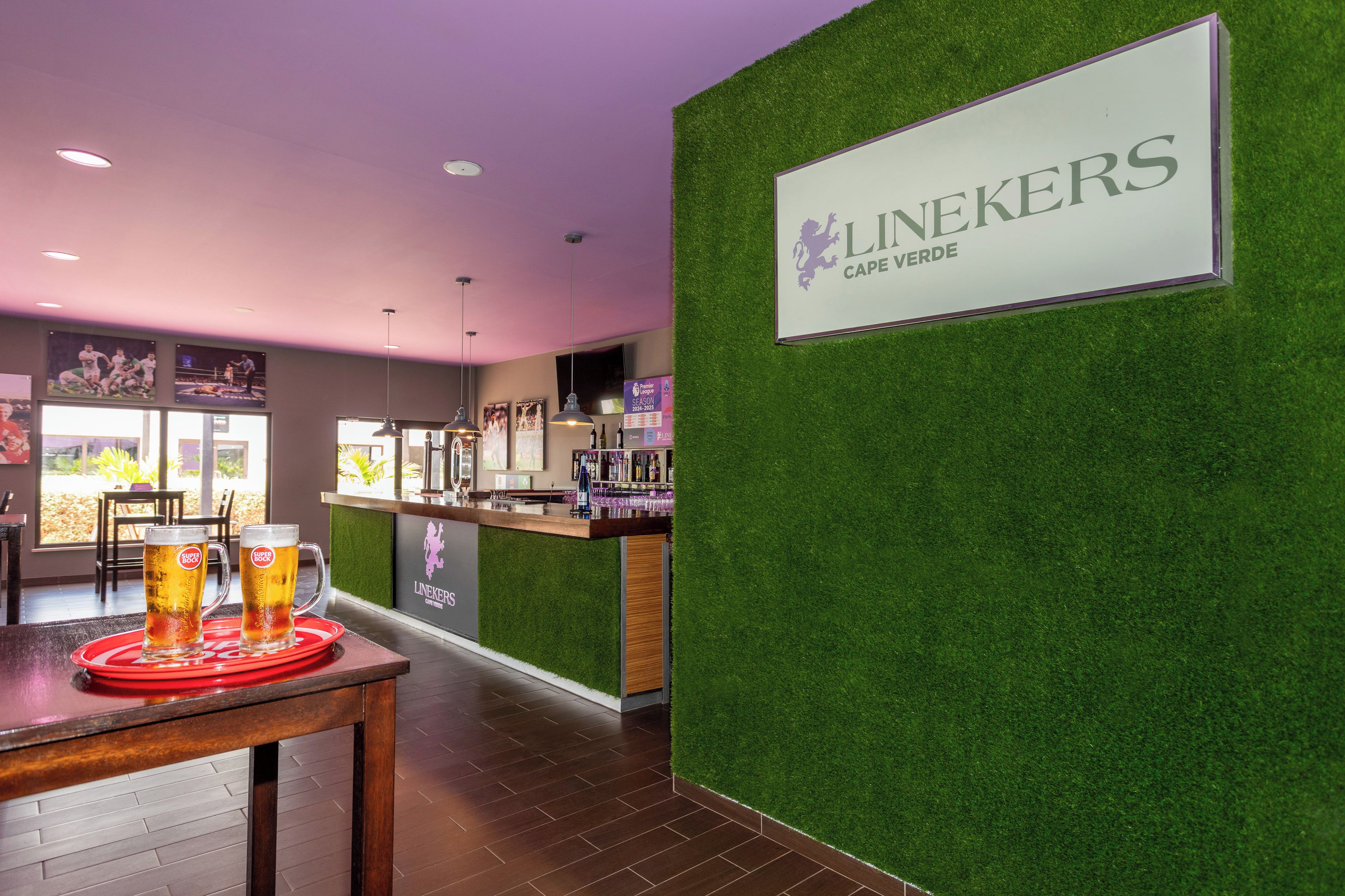 A bar area with a sign for Linekers Cape Verde, a bar counter, and a table with a beer mug.
