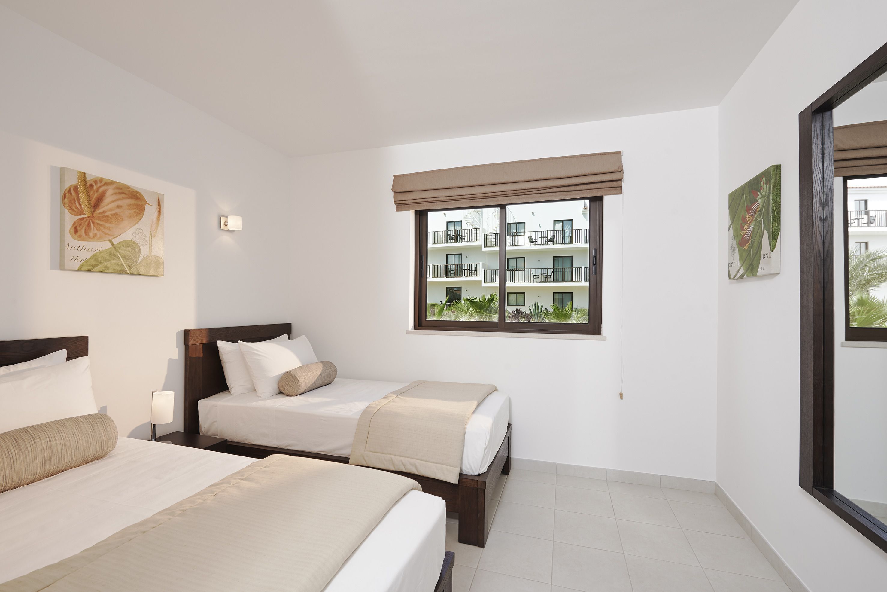 Habitación de hotel con dos camas, un ventanal con vistas a otros edificios y obras de arte en las paredes.