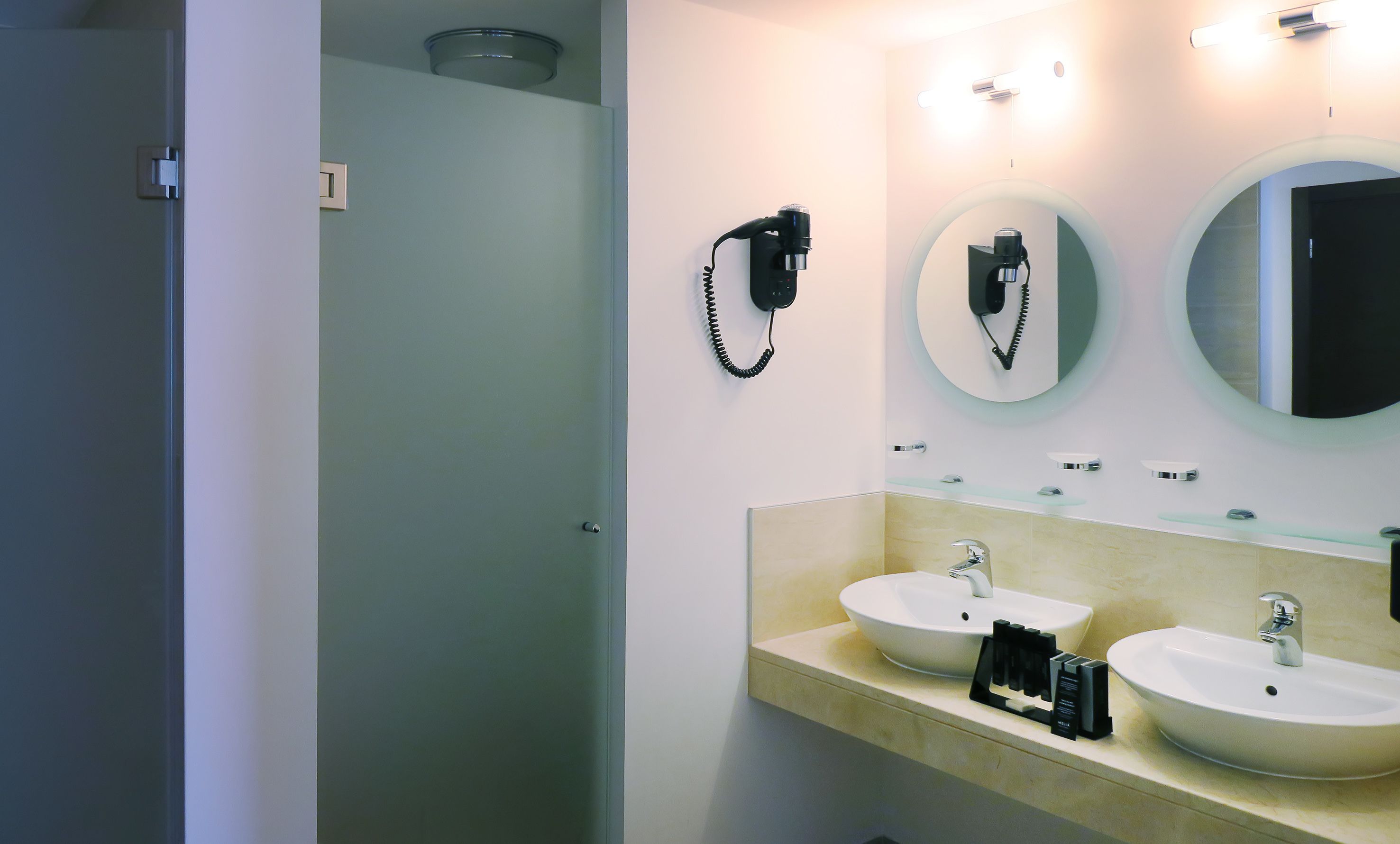 Un baño moderno con dos lavabos, un secador de pelo y un espejo.