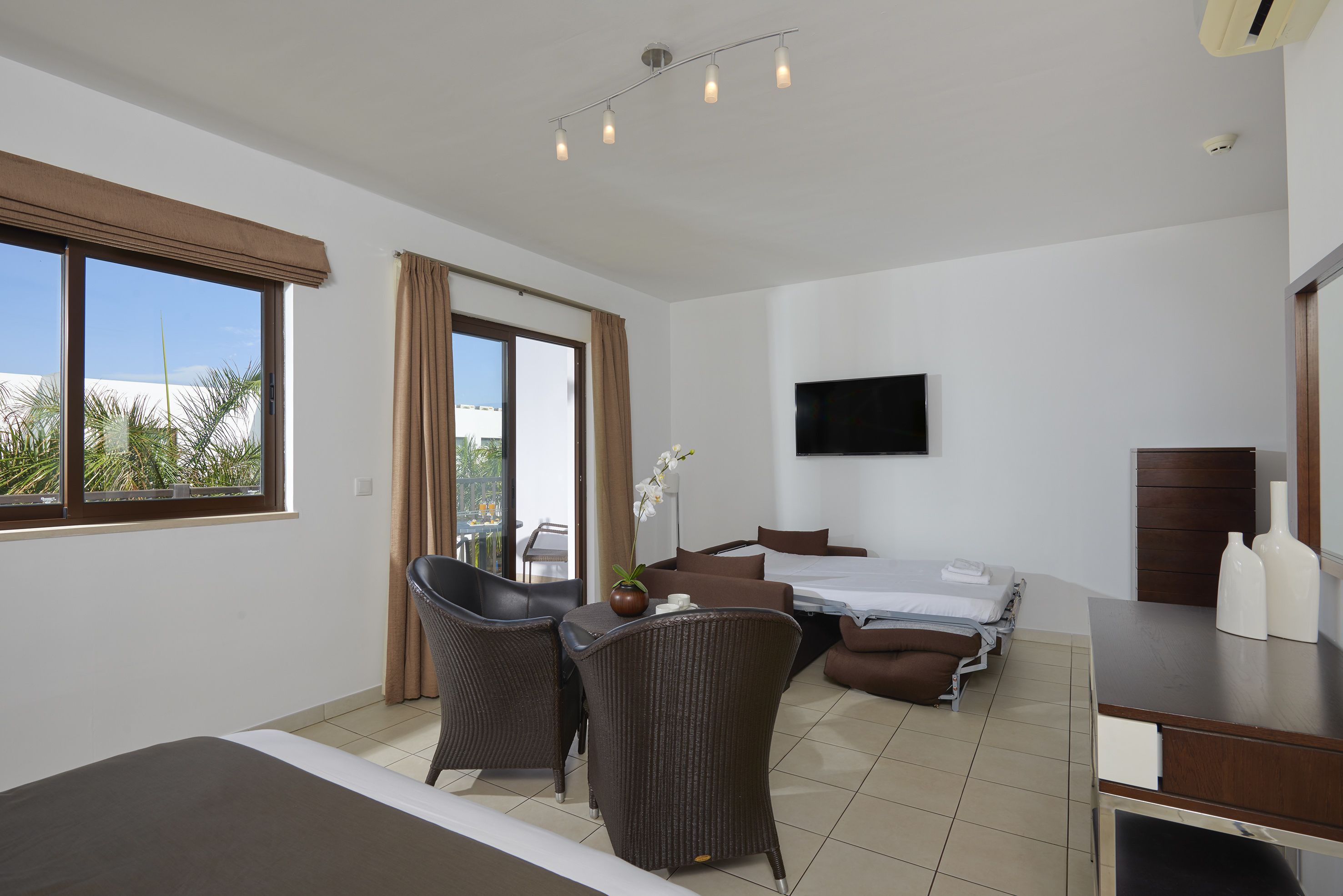 A hotel room with a bed, a desk, a chair, a TV, and a window with curtains.