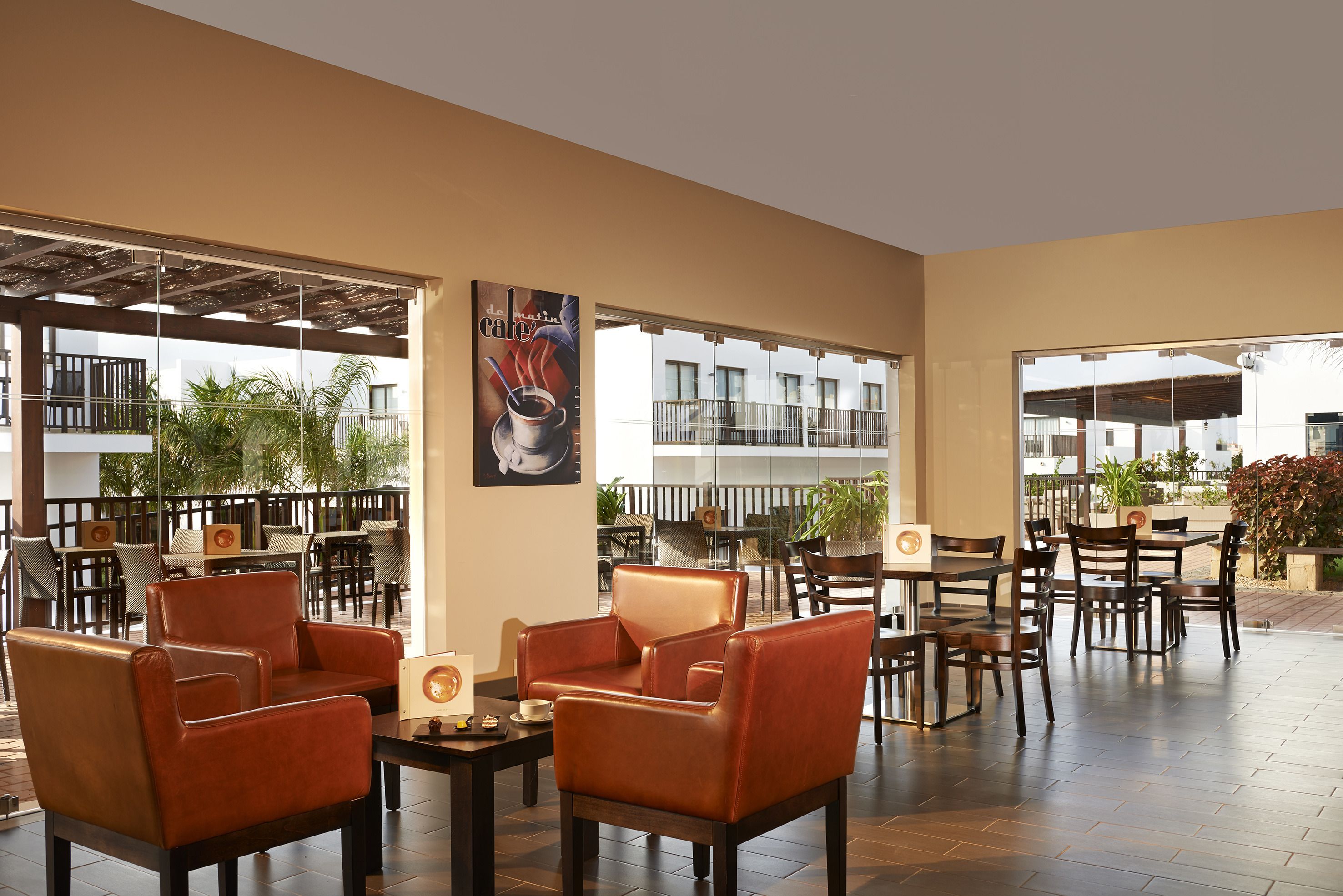 A spacious indoor seating area with leather chairs and tables, large windows offering views of the surrounding buildings and greenery.