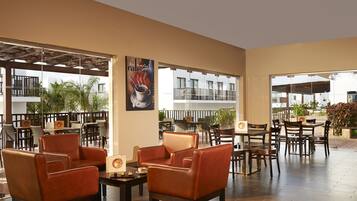 A spacious indoor seating area with leather chairs and tables, large windows offering views of the surrounding buildings and greenery.