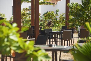 An outdoor patio area with wicker furniture and a view of a white building in the background. - Melia Dunas Beach Resort & Spa - All Inclusive (Sal)