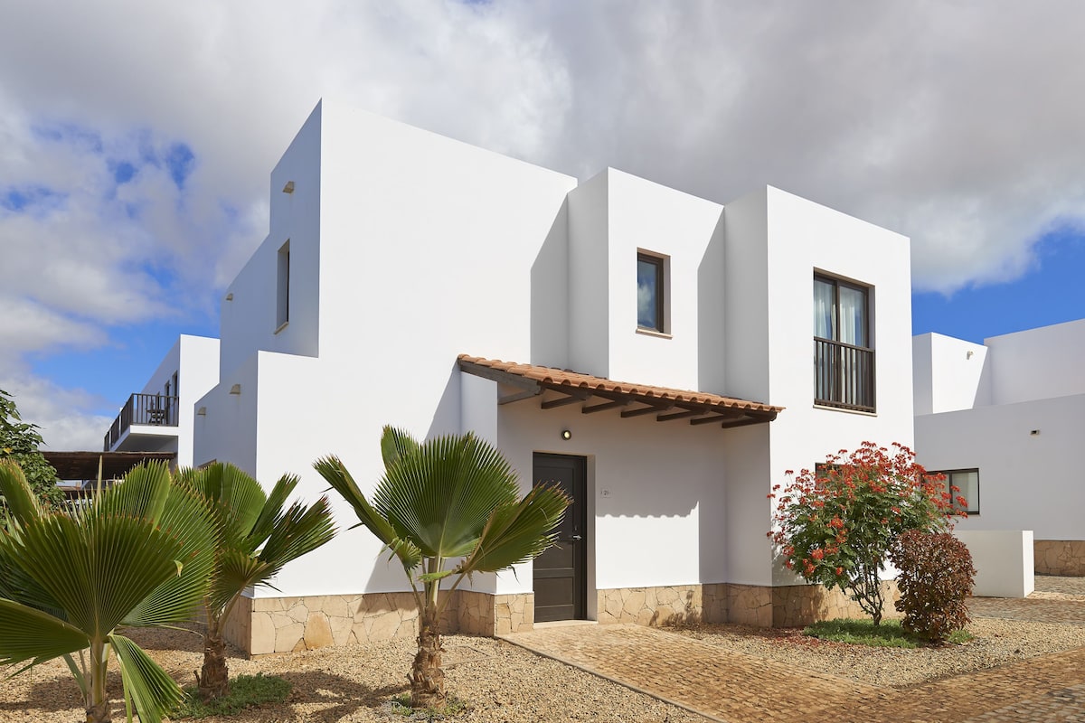 A modern white building with a flat roof, a small balcony, and a door.