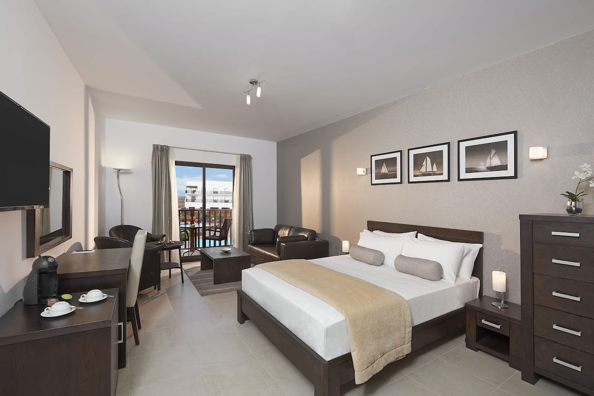 A hotel room with a bed, a desk, a chair, a dresser, and a balcony with a view.