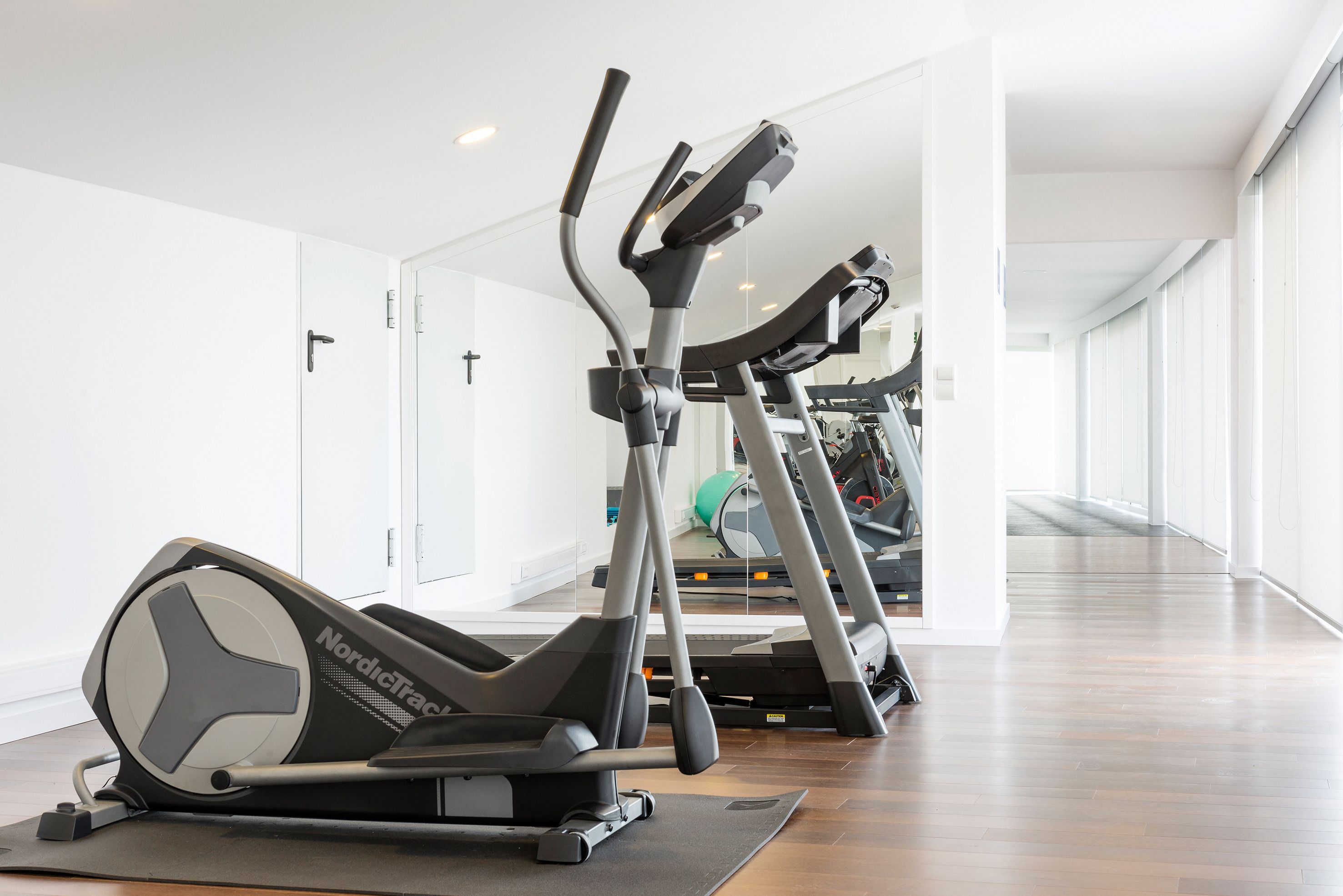 Un gimnasio con máquinas de cardio, un espejo y suelo de madera.