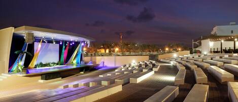 Espacio al aire libre nocturno con fuente de agua, asientos y una estructura de edificio moderna.