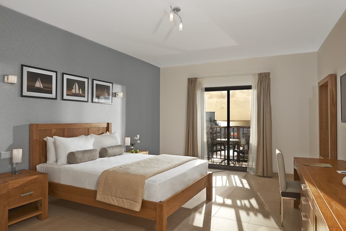 A modern hotel room with a wooden bed, a desk, and a balcony with a view.