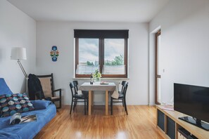 Una sala de estar moderna con una mesa de comedor, sillas, un sofá, un televisor y un ventanal con vistas.