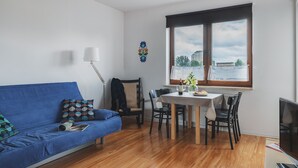 Un soggiorno moderno con un divano blu, un tavolo da pranzo con sedie, una televisione e una finestra con vista sugli edifici.