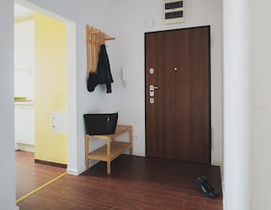 A hallway with a wooden bench, a coat rack with a jacket, a door with a keyhole, and a pair of shoes on the floor. - P&O Apartments Namyslowska (Warsaw)